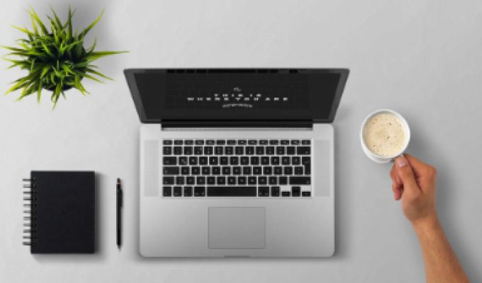 widok z góry otwarty laptop, filiżanka z kawą notatnik i kwiatek doniczkowy