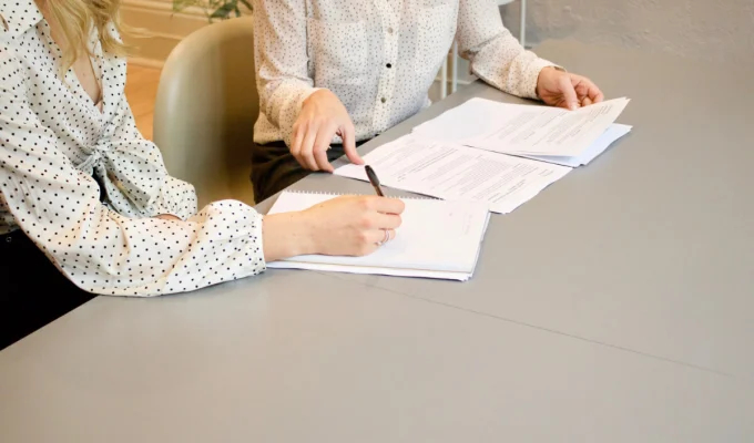 obrazek przedstawia osoby podpisujące dokumenty zbliżenie na ręce