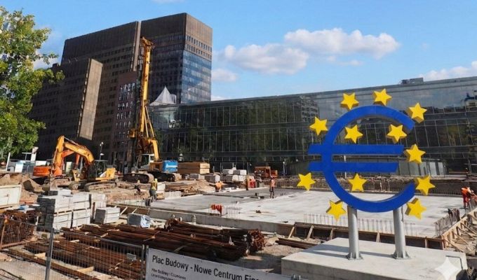 Plac budowy przed szklanym biurowcem, symbol waluty euro toczony żółtymi gwiazdkami