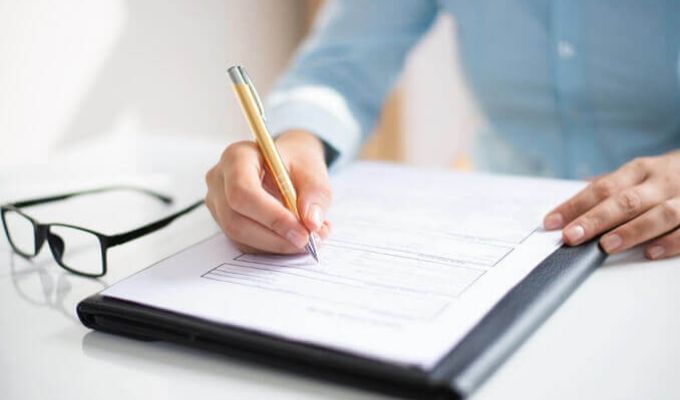 obok kartki paperu leżą okularyosoba pisze coś na kartce zblizenie na kartkę i ręce