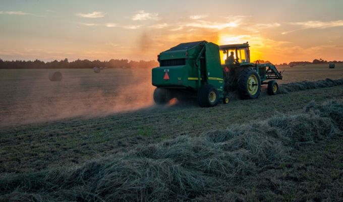 traktor ciągnący po polu belarkę do siana